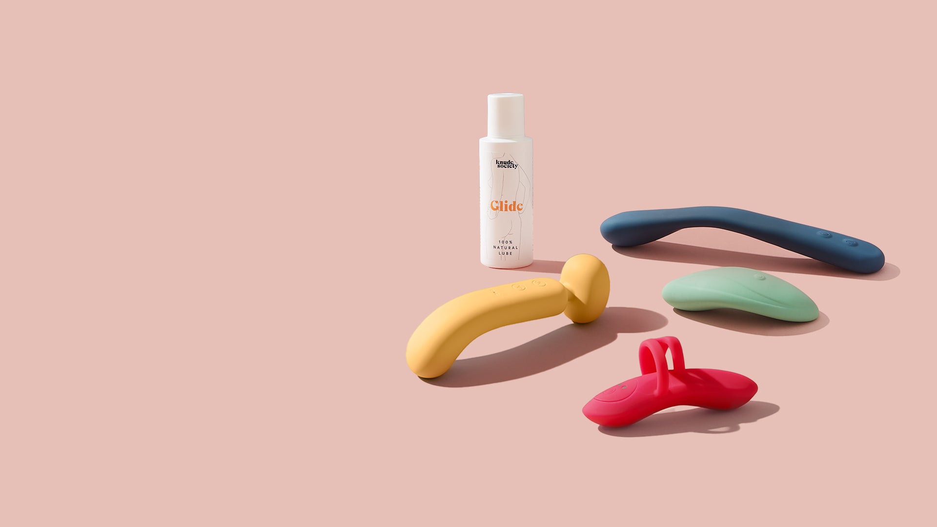 Collection of colorful silicone toys on a pink background with a bottle labeled 'Glide'.